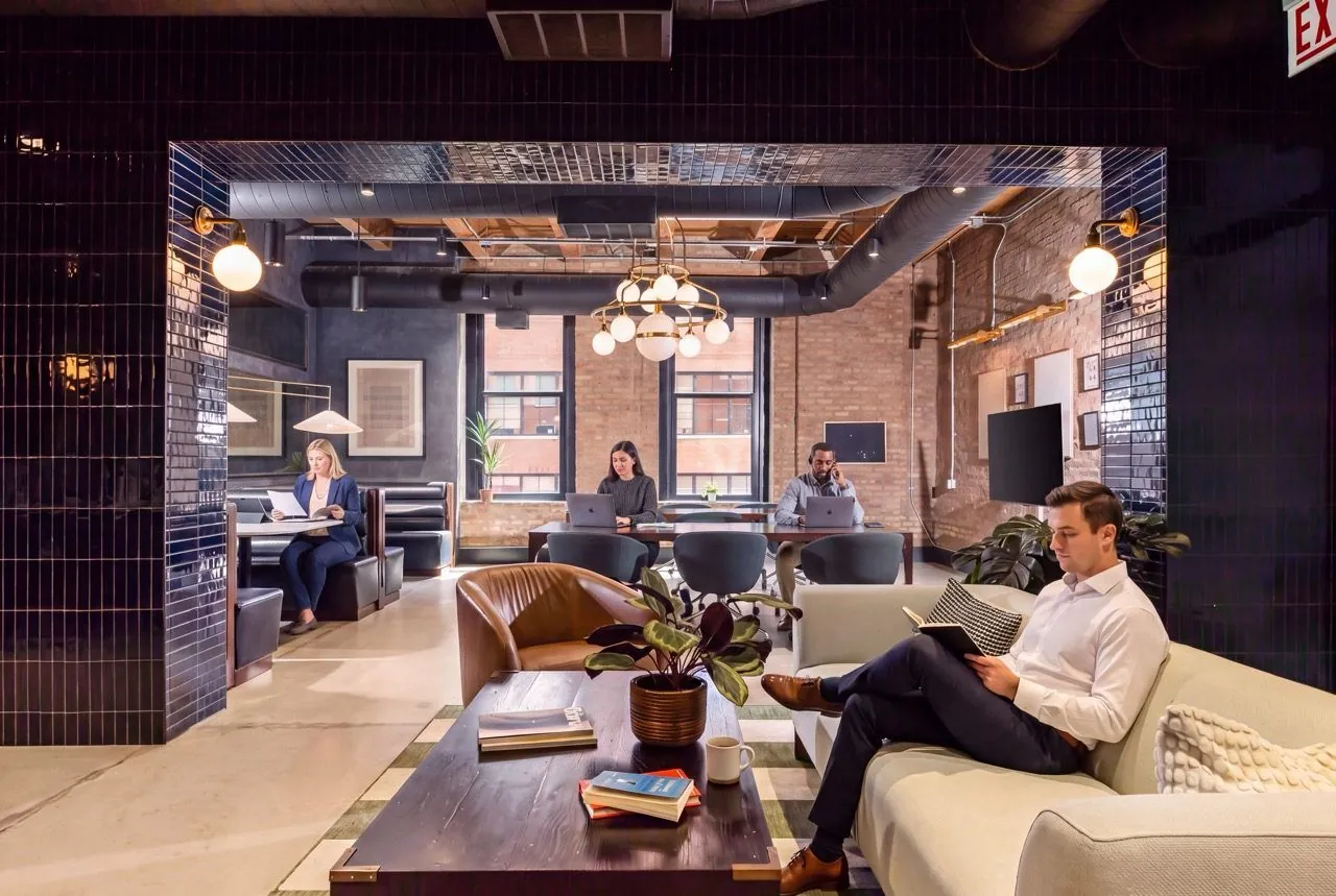 Members working across the coworking lounge—banquette booths, a shared table, and soft seating under globe pendants and navy tile