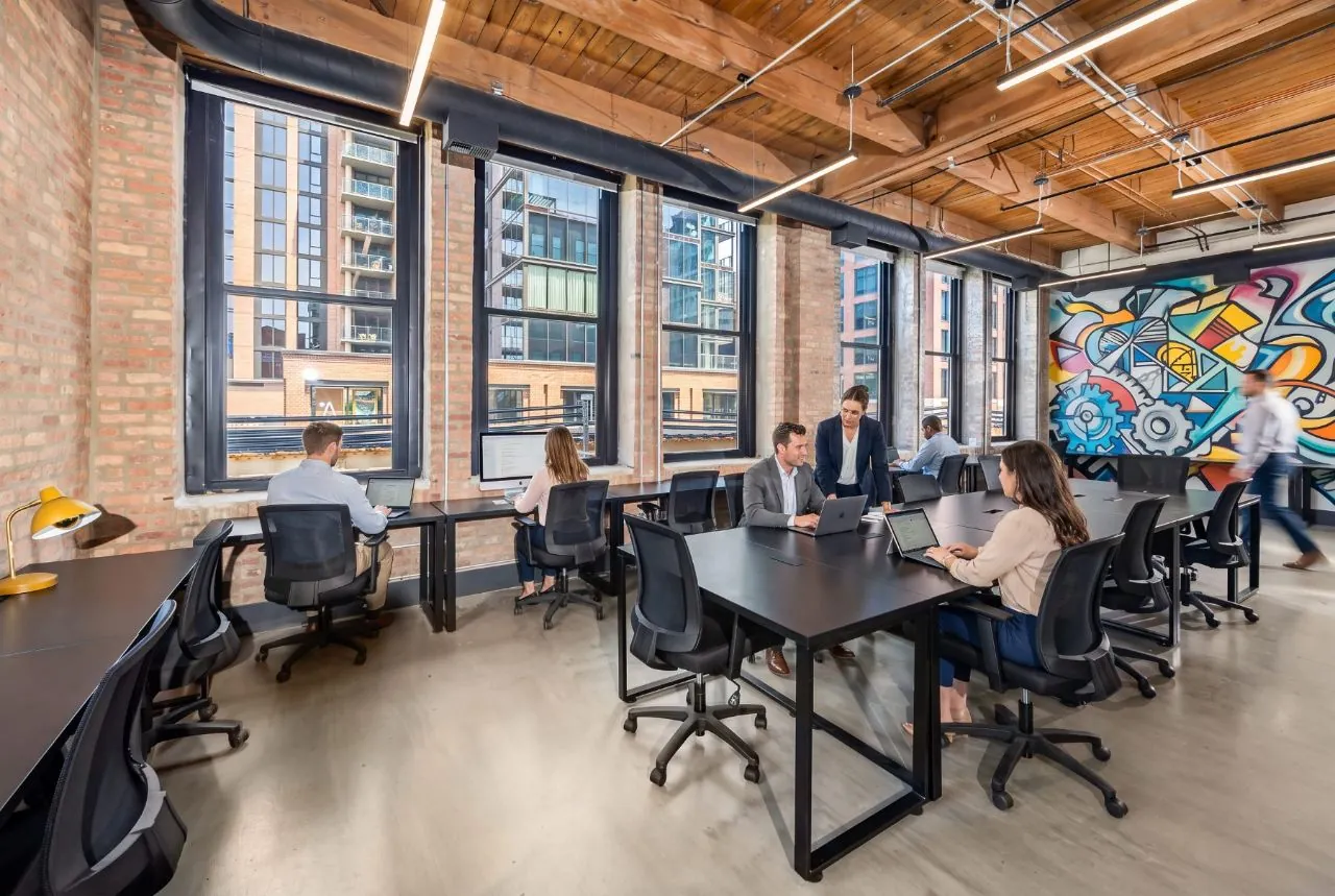 Enterprise suite with a full team at work—brick columns, timber ceilings, industrial windows, and a colorful mural