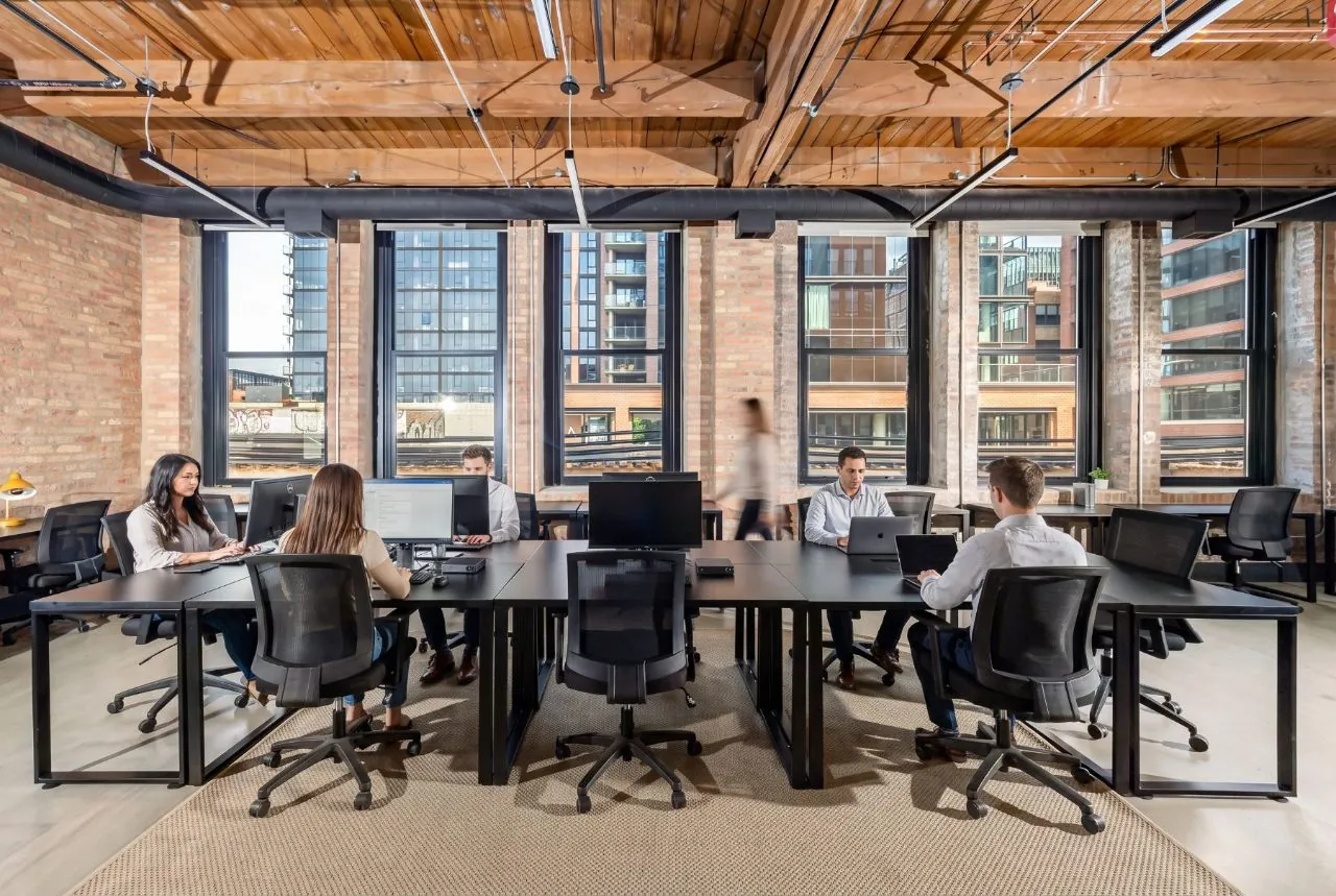 Team suite with members at black workstations, timber ceilings, and industrial windows overlooking Fulton Market