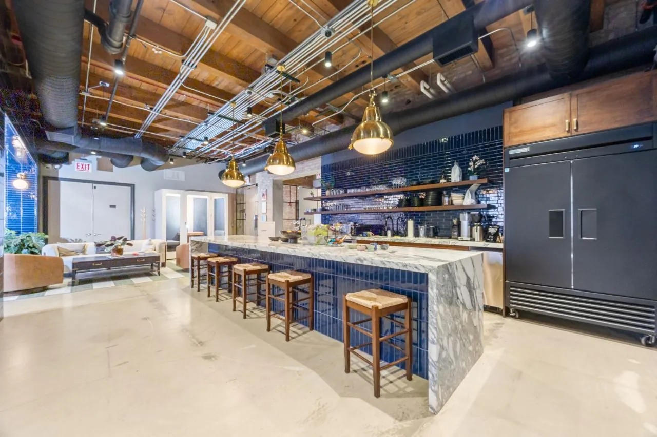 Marble waterfall kitchen island with navy tile, brass pendant lighting, and timber ceiling